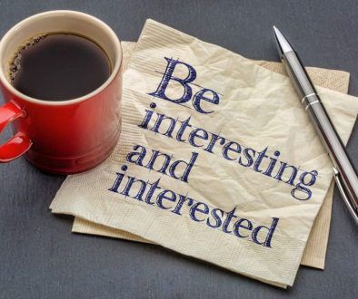 picture of a cup of coffee, a pen, and a napkin that reads "be interesting and interested"