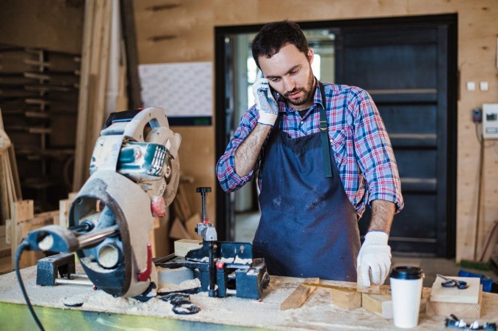 portrait of carpenter calling by smart phone at the workshop.